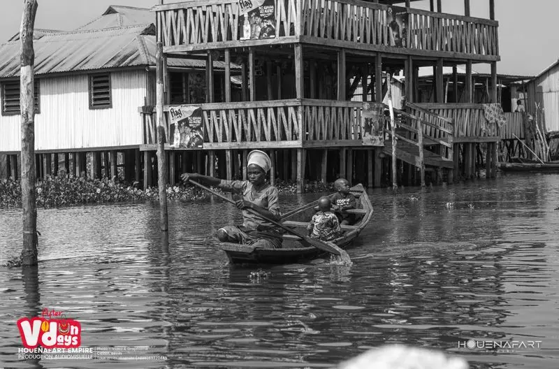 Mujer remando con sus hijos frente a una casa de dos plantas sobre pilotes, Ganvié, ciudad lacustre del lago Nokoué, Benín